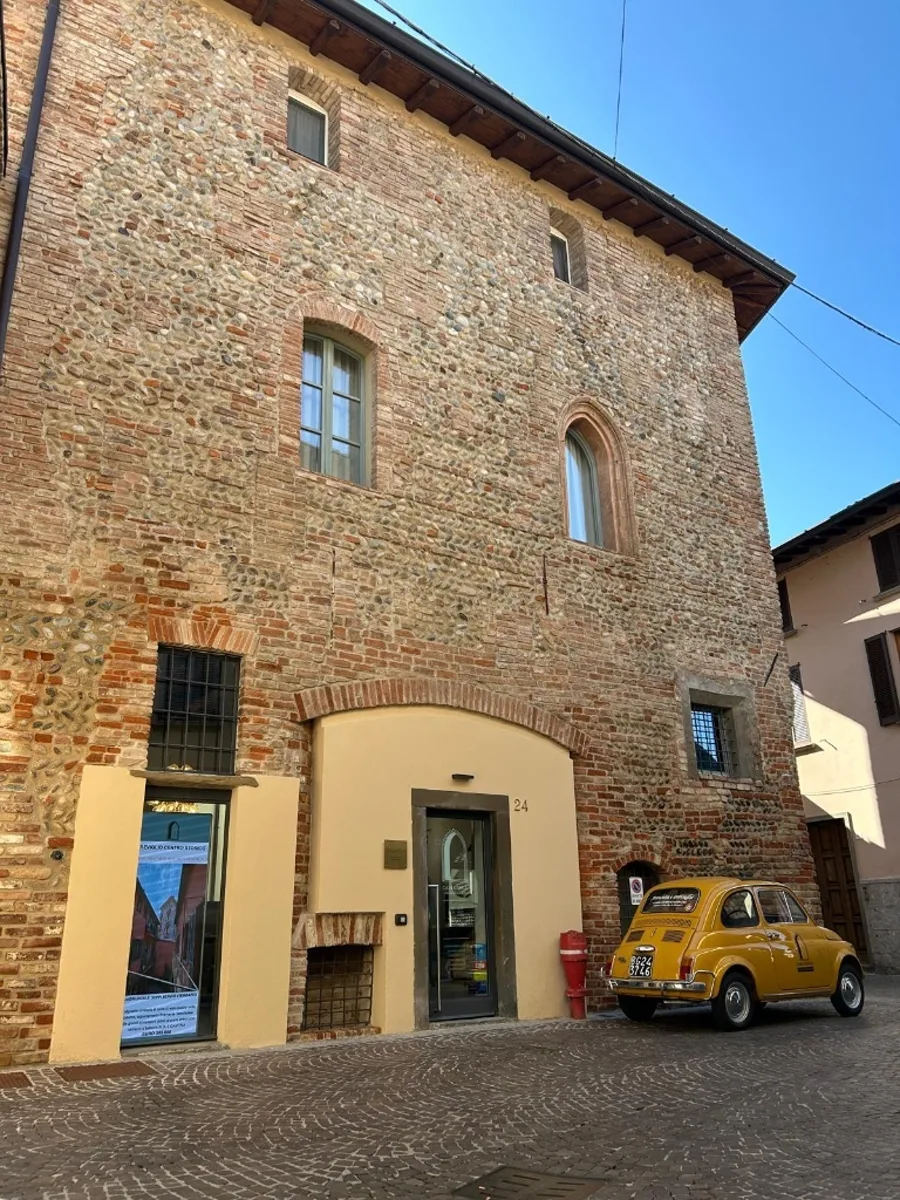 La sede di Casa Gotica: il palazzo storico in mattoni con la Fiat 500 gialla dell'agenzia parcheggiata davanti all'ingresso